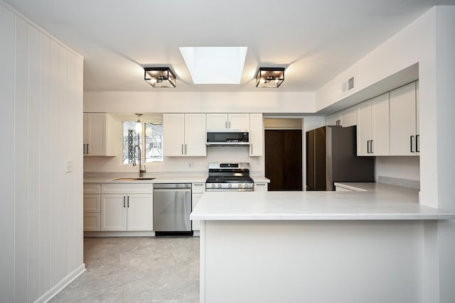 kitchen with a skylight, white cabinetry, sink, and stainless steel appliances