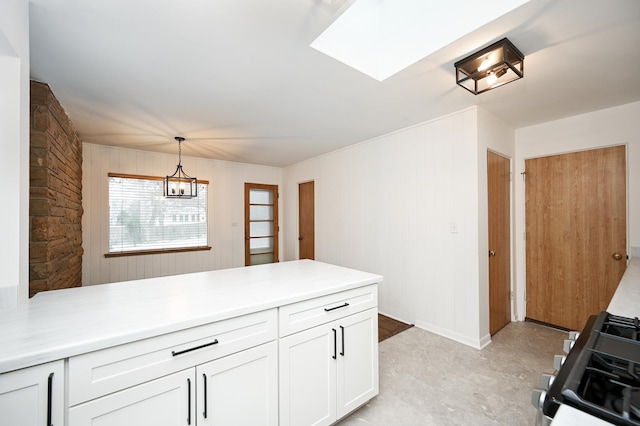 kitchen featuring kitchen peninsula, white cabinets, range, hanging light fixtures, and wood walls