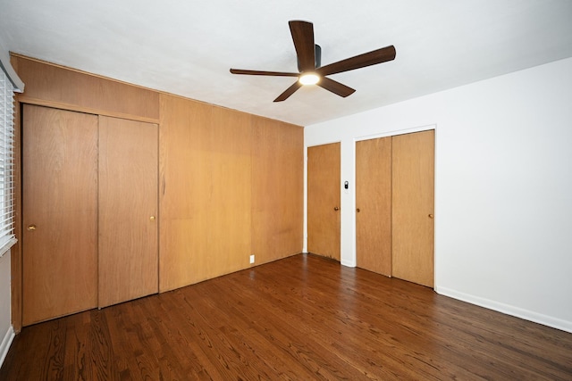 unfurnished bedroom with multiple closets, ceiling fan, and dark hardwood / wood-style floors