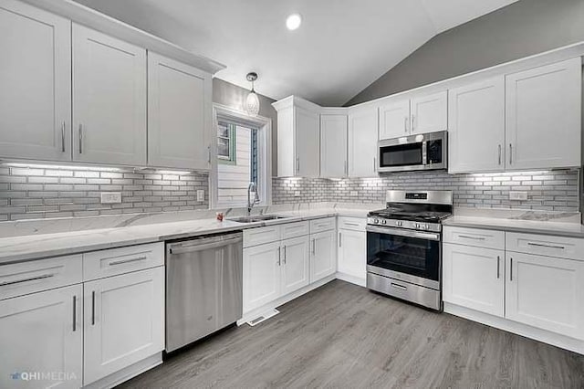 kitchen with white cabinetry, hanging light fixtures, stainless steel appliances, and vaulted ceiling