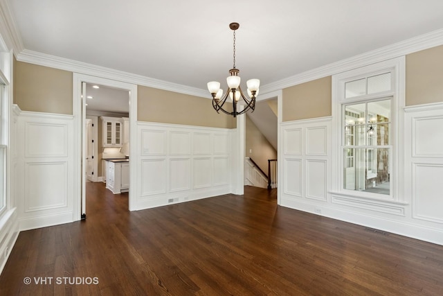 unfurnished dining area featuring dark hardwood / wood-style floors, ornamental molding, and a notable chandelier