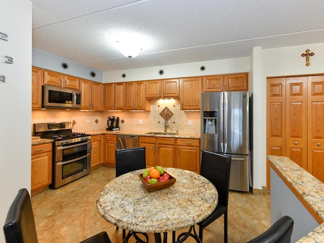 kitchen with a textured ceiling, light stone countertops, stainless steel appliances, and tasteful backsplash