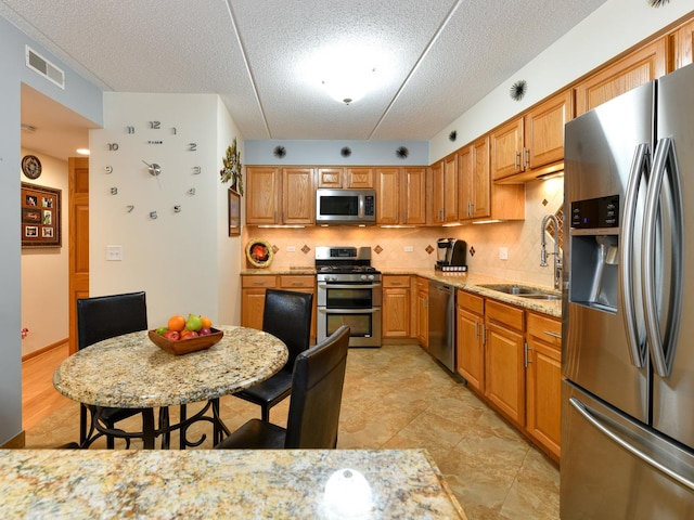 kitchen featuring sink, tasteful backsplash, light stone counters, a textured ceiling, and appliances with stainless steel finishes