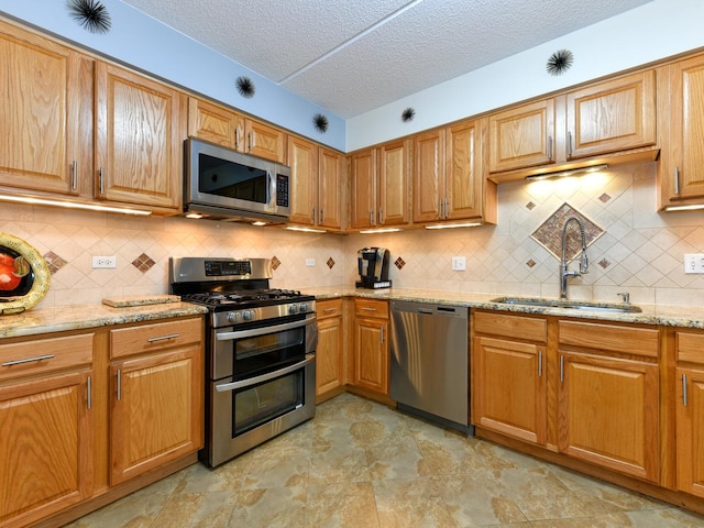 kitchen featuring sink, tasteful backsplash, light stone counters, a textured ceiling, and appliances with stainless steel finishes