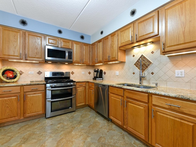 kitchen with decorative backsplash, light stone countertops, a textured ceiling, stainless steel appliances, and sink