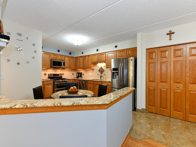 kitchen featuring kitchen peninsula, appliances with stainless steel finishes, tasteful backsplash, and light stone countertops