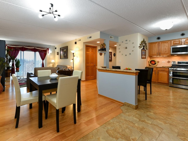 dining room with light hardwood / wood-style floors, a textured ceiling, and a notable chandelier