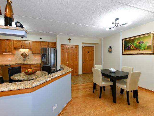 kitchen with light stone counters, stainless steel fridge, a chandelier, decorative backsplash, and light wood-type flooring