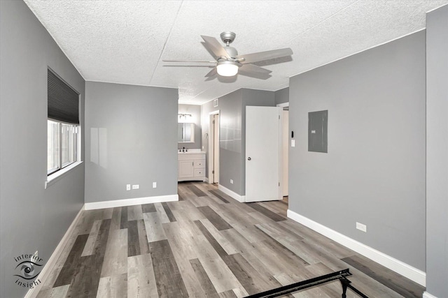 unfurnished living room with a textured ceiling, electric panel, light hardwood / wood-style flooring, and ceiling fan