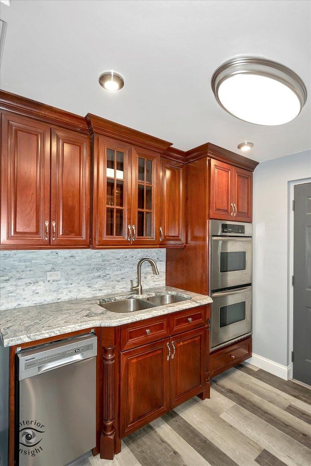 kitchen with backsplash, sink, light stone countertops, light hardwood / wood-style floors, and stainless steel appliances