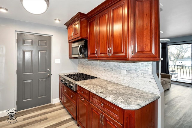 kitchen with light stone countertops, stainless steel appliances, light hardwood / wood-style flooring, and tasteful backsplash