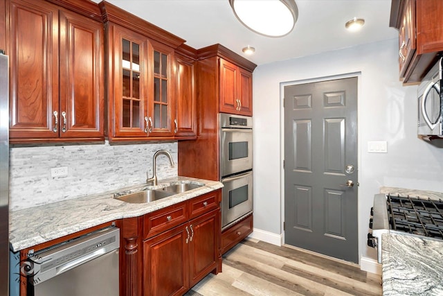 kitchen with light stone countertops, sink, appliances with stainless steel finishes, and light hardwood / wood-style flooring