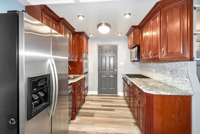 kitchen with sink, tasteful backsplash, light hardwood / wood-style floors, light stone counters, and stainless steel appliances