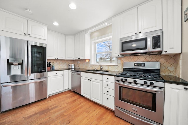 kitchen featuring appliances with stainless steel finishes, tasteful backsplash, sink, light hardwood / wood-style floors, and white cabinetry