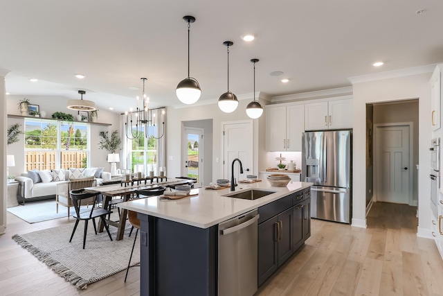 kitchen featuring stainless steel appliances, a kitchen island with sink, sink, decorative light fixtures, and white cabinetry