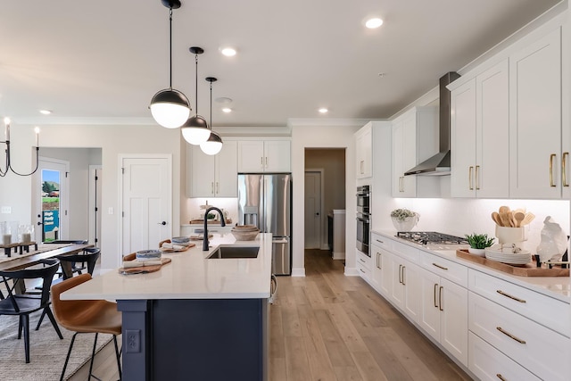 kitchen with wall chimney exhaust hood, stainless steel appliances, sink, white cabinets, and an island with sink