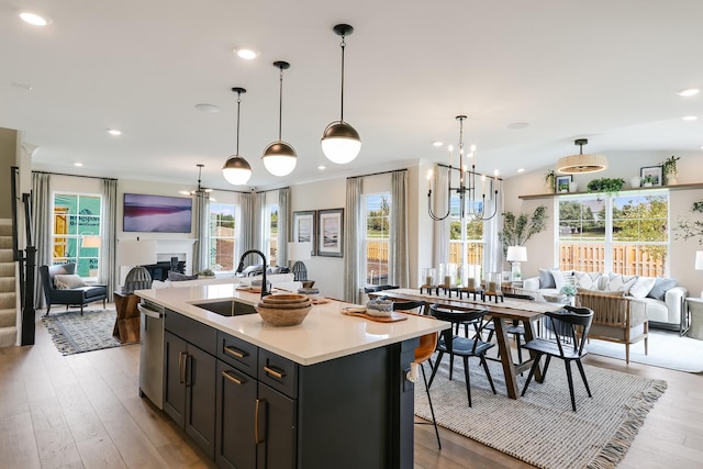 kitchen with stainless steel dishwasher, vaulted ceiling, sink, decorative light fixtures, and an island with sink