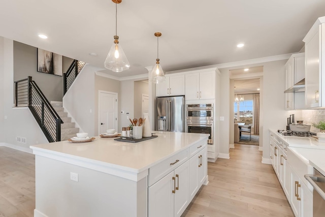 kitchen with white cabinetry, a center island, decorative light fixtures, appliances with stainless steel finishes, and light wood-type flooring