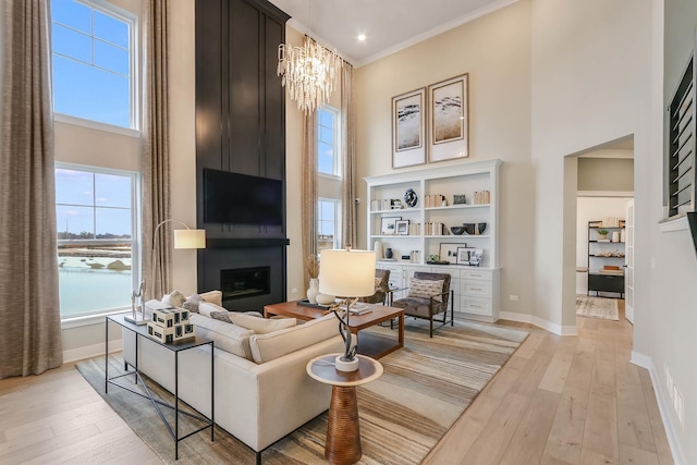 living room featuring a notable chandelier, light wood-type flooring, a fireplace, and ornamental molding