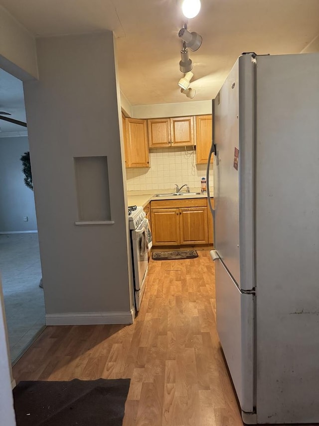 kitchen with appliances with stainless steel finishes, light brown cabinetry, tasteful backsplash, sink, and light hardwood / wood-style flooring