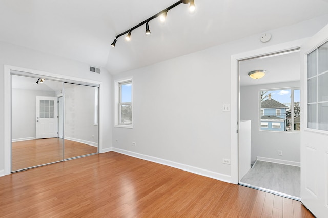 unfurnished bedroom featuring hardwood / wood-style floors, rail lighting, a closet, and lofted ceiling