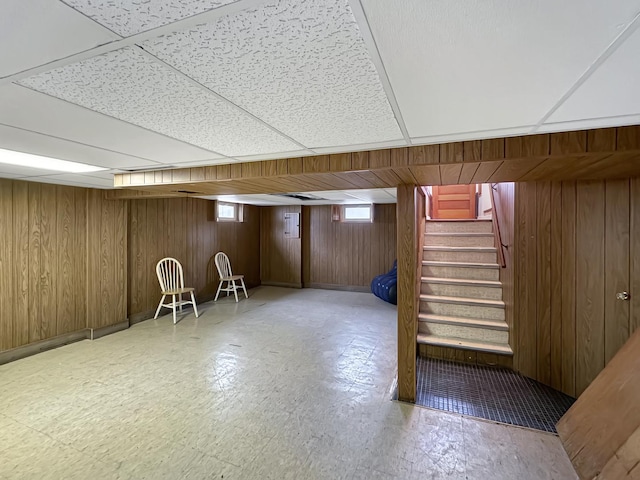 basement with a drop ceiling and wooden walls