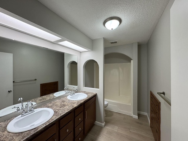 full bathroom with shower / bathtub combination, a textured ceiling, vanity, hardwood / wood-style flooring, and toilet