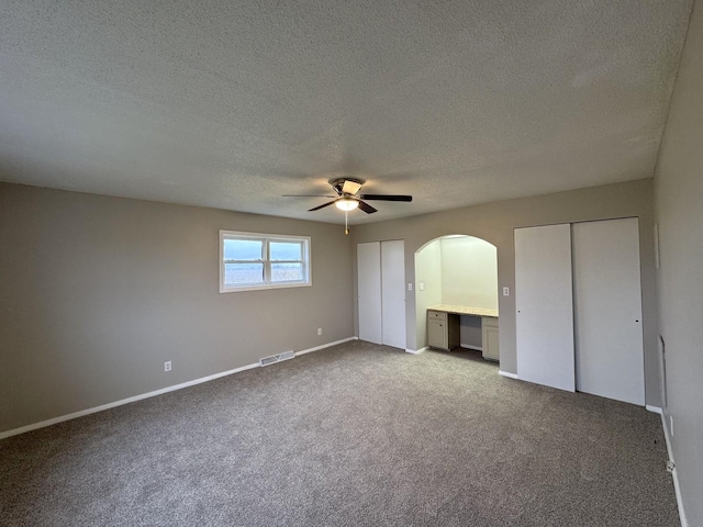 unfurnished bedroom with two closets, a textured ceiling, light colored carpet, and ceiling fan