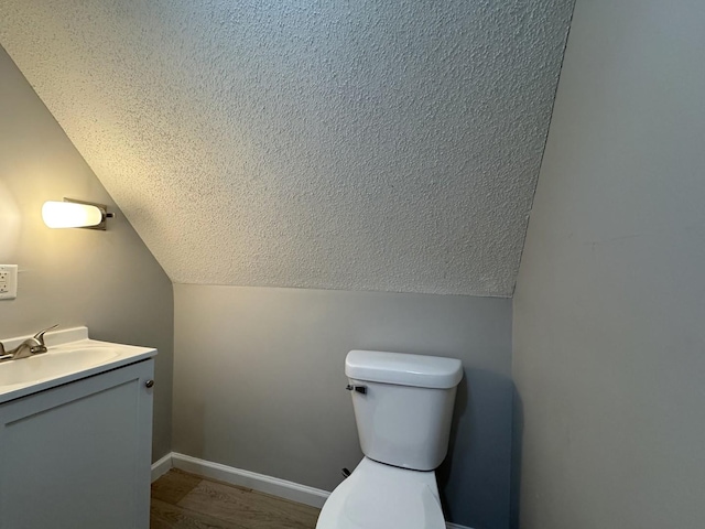 bathroom featuring wood-type flooring, vanity, toilet, and lofted ceiling