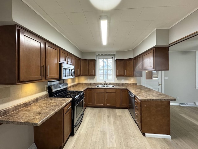 kitchen with kitchen peninsula, dark brown cabinetry, stainless steel appliances, sink, and light hardwood / wood-style flooring