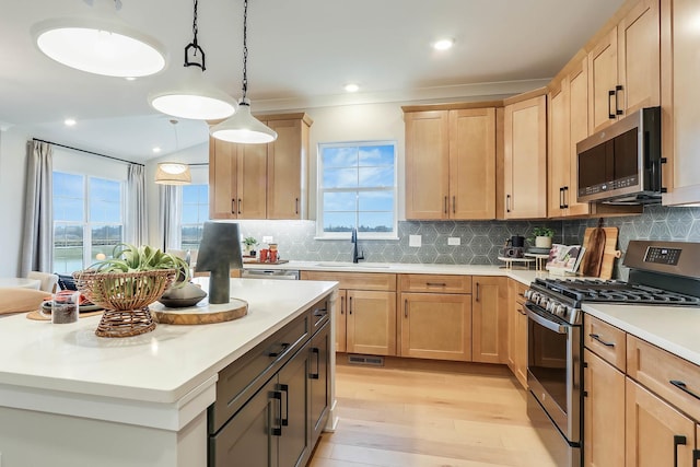 kitchen with light brown cabinets, sink, hanging light fixtures, light wood-type flooring, and appliances with stainless steel finishes