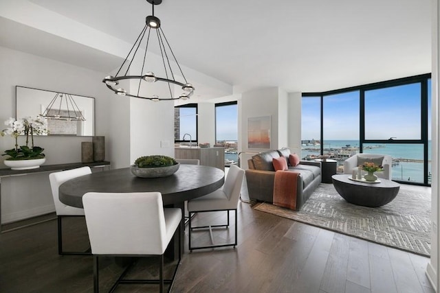 dining area featuring floor to ceiling windows, an inviting chandelier, a water view, sink, and dark hardwood / wood-style floors