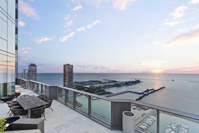 balcony at dusk featuring a water view