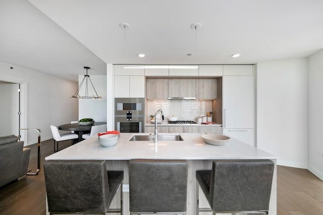 kitchen featuring a center island with sink, decorative light fixtures, sink, and hardwood / wood-style flooring