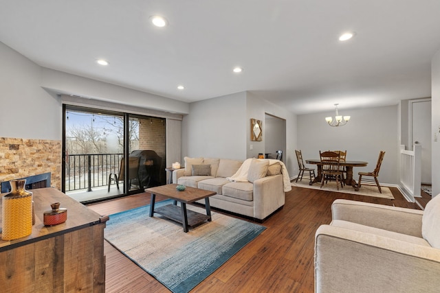 living room featuring dark hardwood / wood-style floors, a stone fireplace, and a notable chandelier