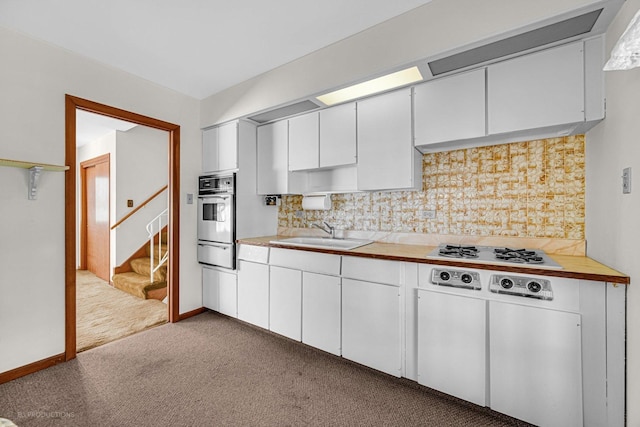 kitchen with sink, light colored carpet, white gas stovetop, and white cabinets