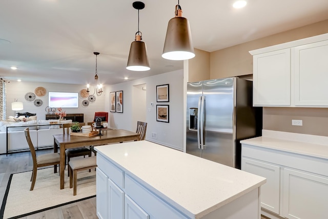 kitchen featuring white cabinetry, hanging light fixtures, a notable chandelier, stainless steel fridge, and light wood-type flooring