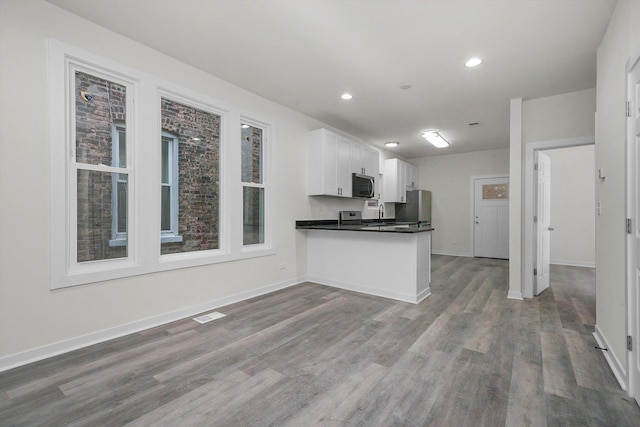 kitchen featuring white cabinets, appliances with stainless steel finishes, hardwood / wood-style flooring, and kitchen peninsula