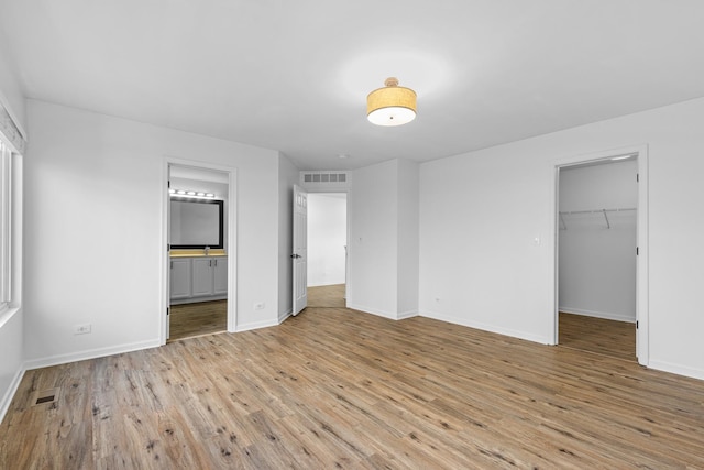 unfurnished bedroom with ensuite bath, a spacious closet, a closet, and light wood-type flooring