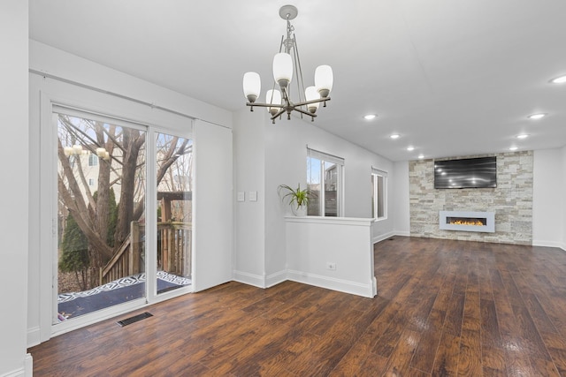 unfurnished living room featuring a notable chandelier, dark hardwood / wood-style floors, and a stone fireplace