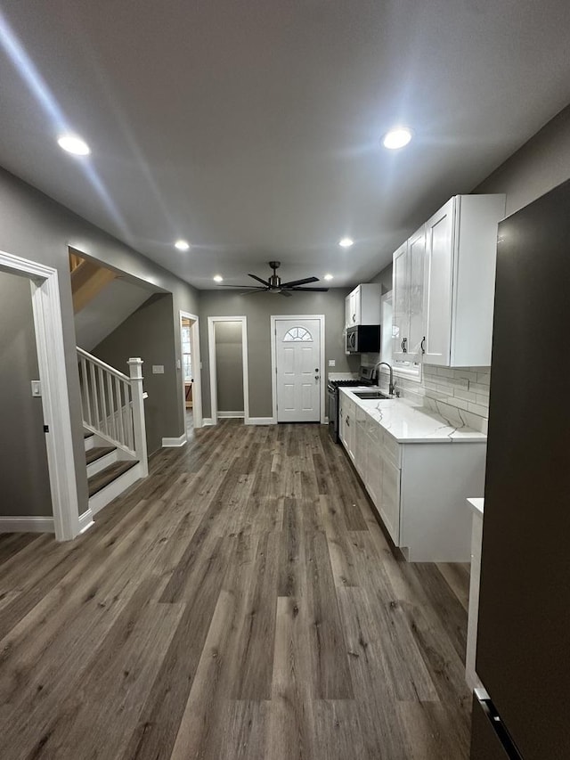 kitchen with white cabinetry, ceiling fan, light stone counters, wood-type flooring, and decorative backsplash