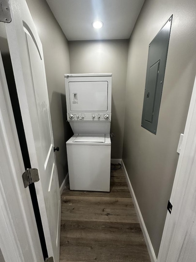 laundry area featuring stacked washer / drying machine, dark hardwood / wood-style flooring, and electric panel