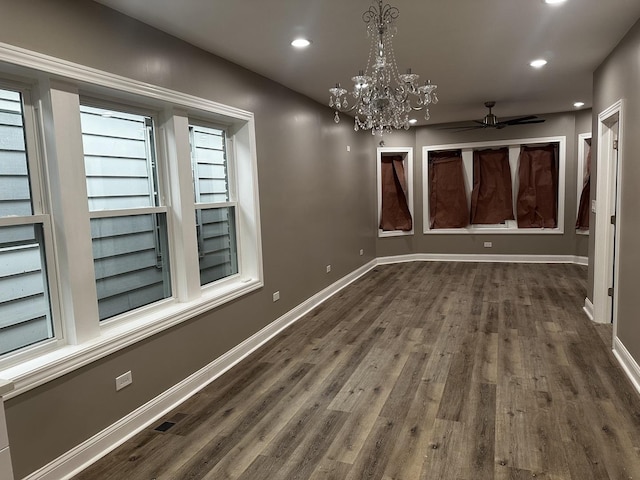 empty room with ceiling fan with notable chandelier and dark wood-type flooring