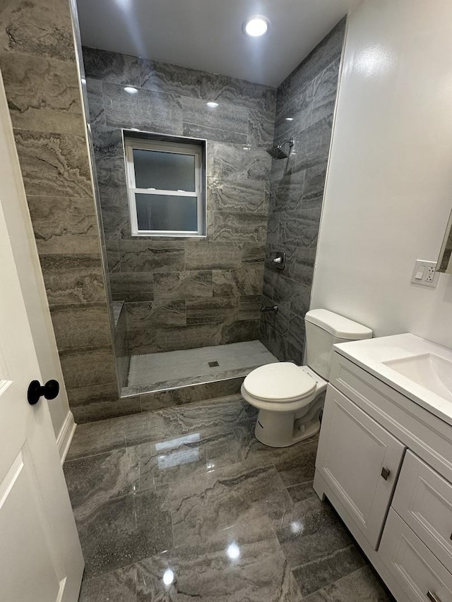 bathroom featuring a tile shower, vanity, and toilet