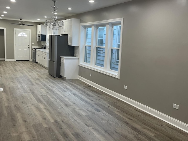 kitchen featuring appliances with stainless steel finishes, light wood-type flooring, ceiling fan with notable chandelier, decorative light fixtures, and white cabinetry