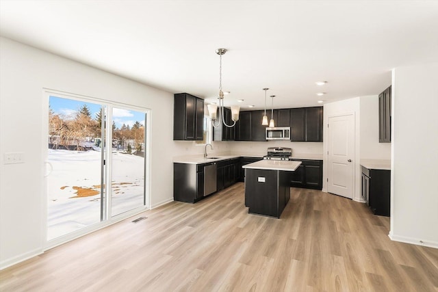 kitchen with stainless steel appliances, a sink, a kitchen island, light countertops, and hanging light fixtures