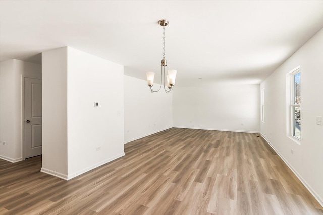 empty room with a notable chandelier, baseboards, and wood finished floors