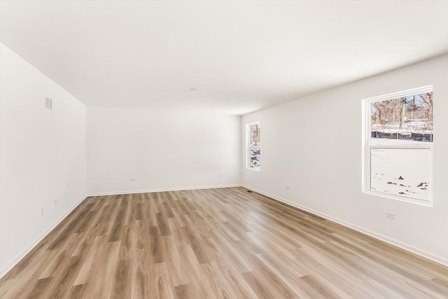 spare room featuring light wood-style floors, a healthy amount of sunlight, and baseboards