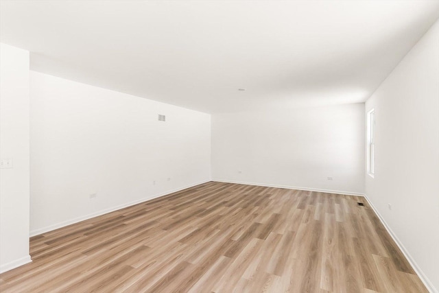 empty room with light wood-type flooring, visible vents, and baseboards