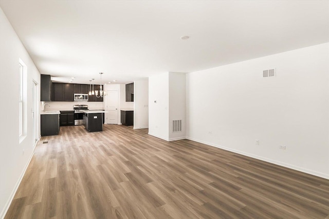 unfurnished living room with wood finished floors, a sink, visible vents, and baseboards